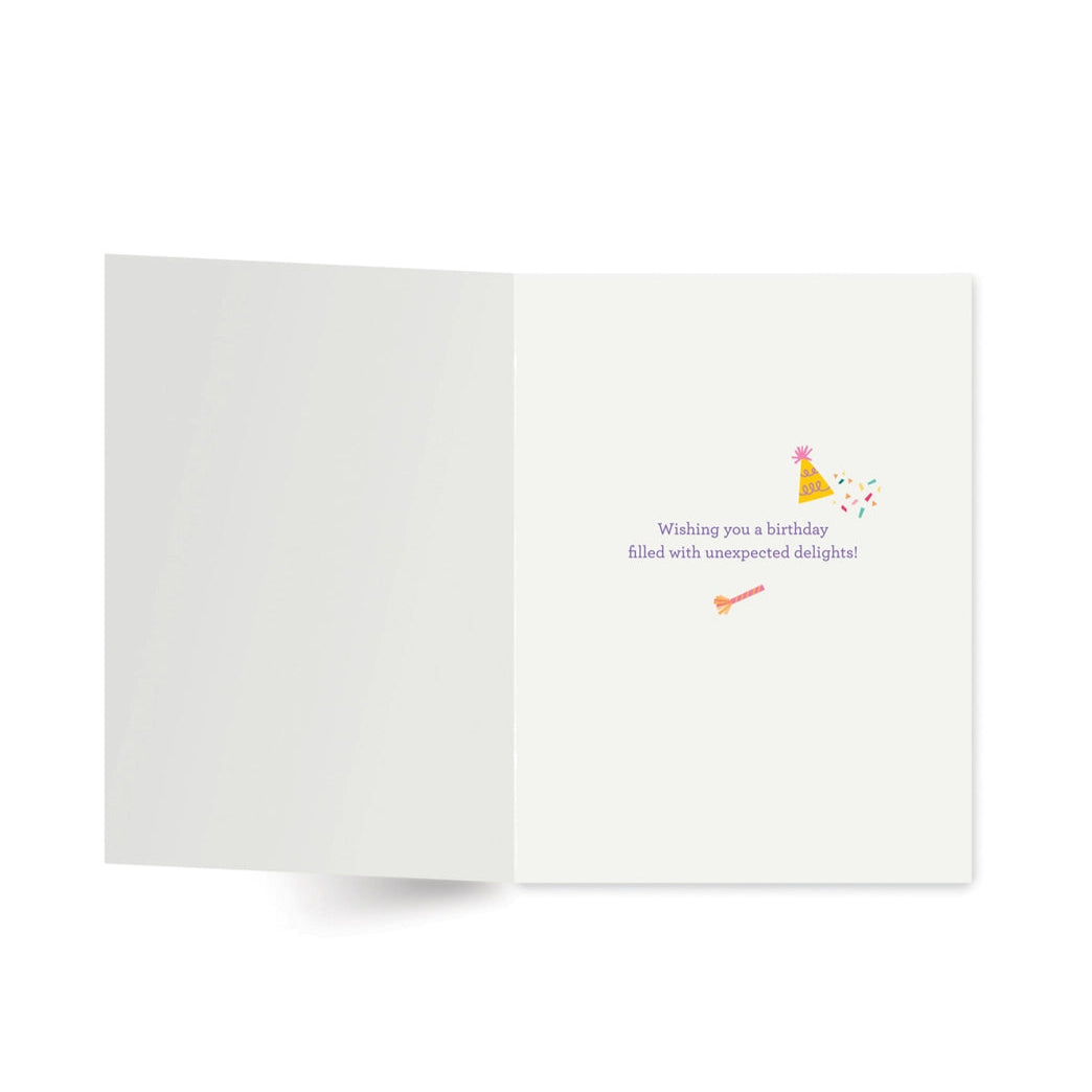 Inside of a white card with a party hat icon and blower and text reading "wishing you a birthday filled with unexpected delights!"
