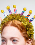 Person wearing a festive headband with colorful candles and tinsel on a plain background