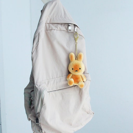Plush bunny keychain attached to a beige backpack against a light blue background