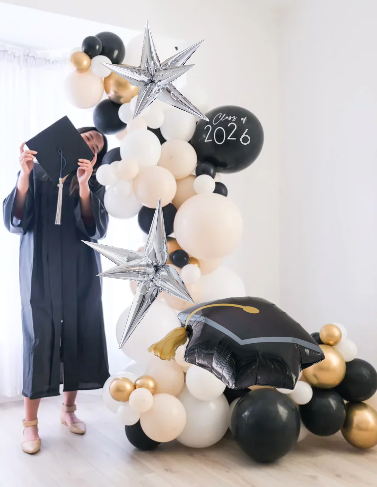 balloon garland with a graduate standing next to it, in black, white, cream and gold colors. starburst balloons are added in.