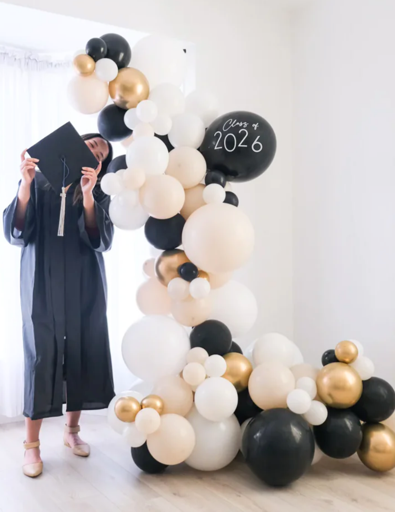 balloon garland with a graduate standing next to it, in balck, white, cream and gold colors