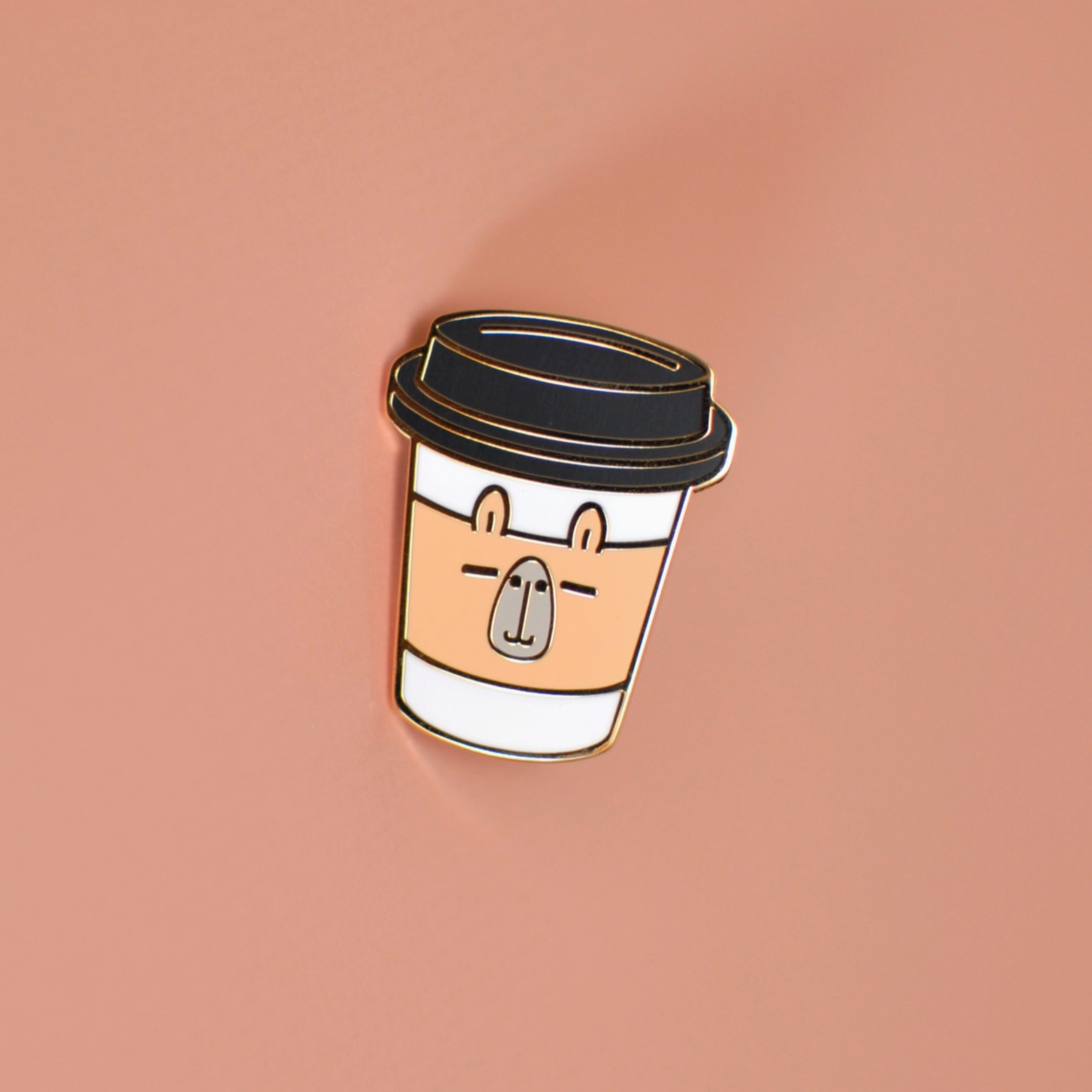 An 18K gold plated enamel pin shaped like a capybara with a coffee cup design on top.