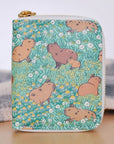 A zipper wallet with a green background featuring illustrations of capybaras among flowers. The wallet has a gold-colored plated brass zipper.