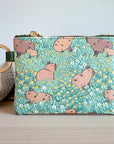 A multicolored coin purse with a brass zipper and a metal key ring, featuring a pattern of capybaras, flowers, and leaves with a fabric accent in the background