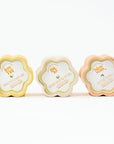 Three floral-shaped candles in pastel colors with labels on a white background