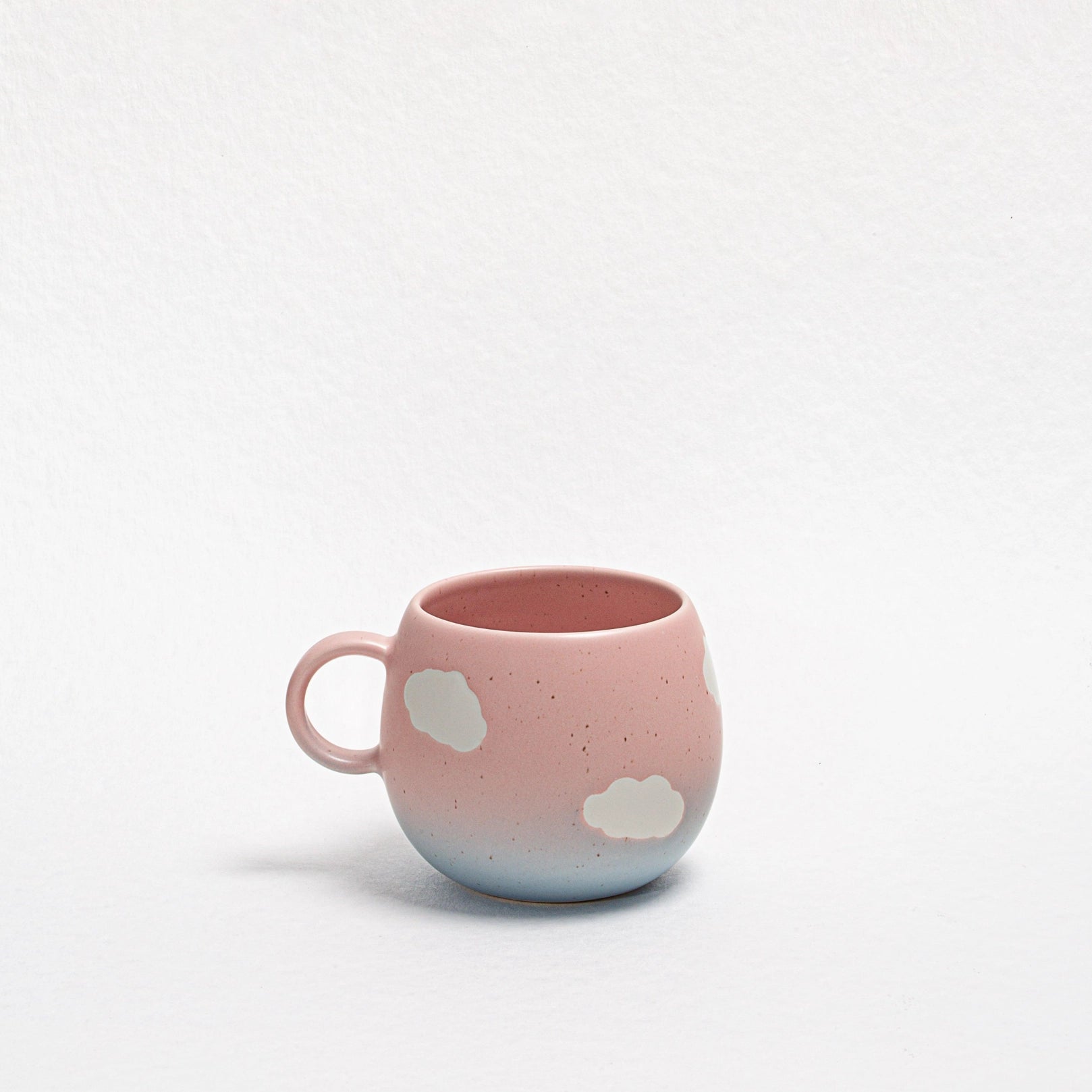 Pink ceramic mug with cloud designs on a light gray background