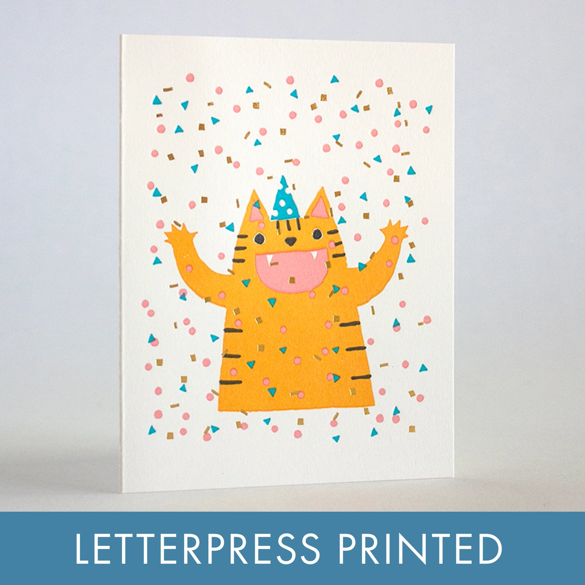 A white greeting card featuring a cute orange tabby cat wearing a blue party hat, surrounded by colorful confetti, shown standing upright against a light gray background. A blue banner at the bottom reads 'LETTERPRESS PRINTED'.