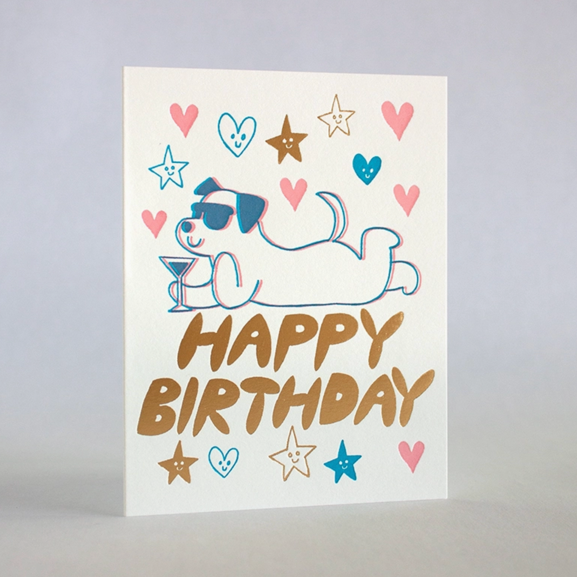 A birthday card with a cartoon illustration of a dog wearing sunglasses and a party hat, reading 'HAPPY BIRTHDAY' in a colorful, retro style design, accompanied by gold foil details and stars.