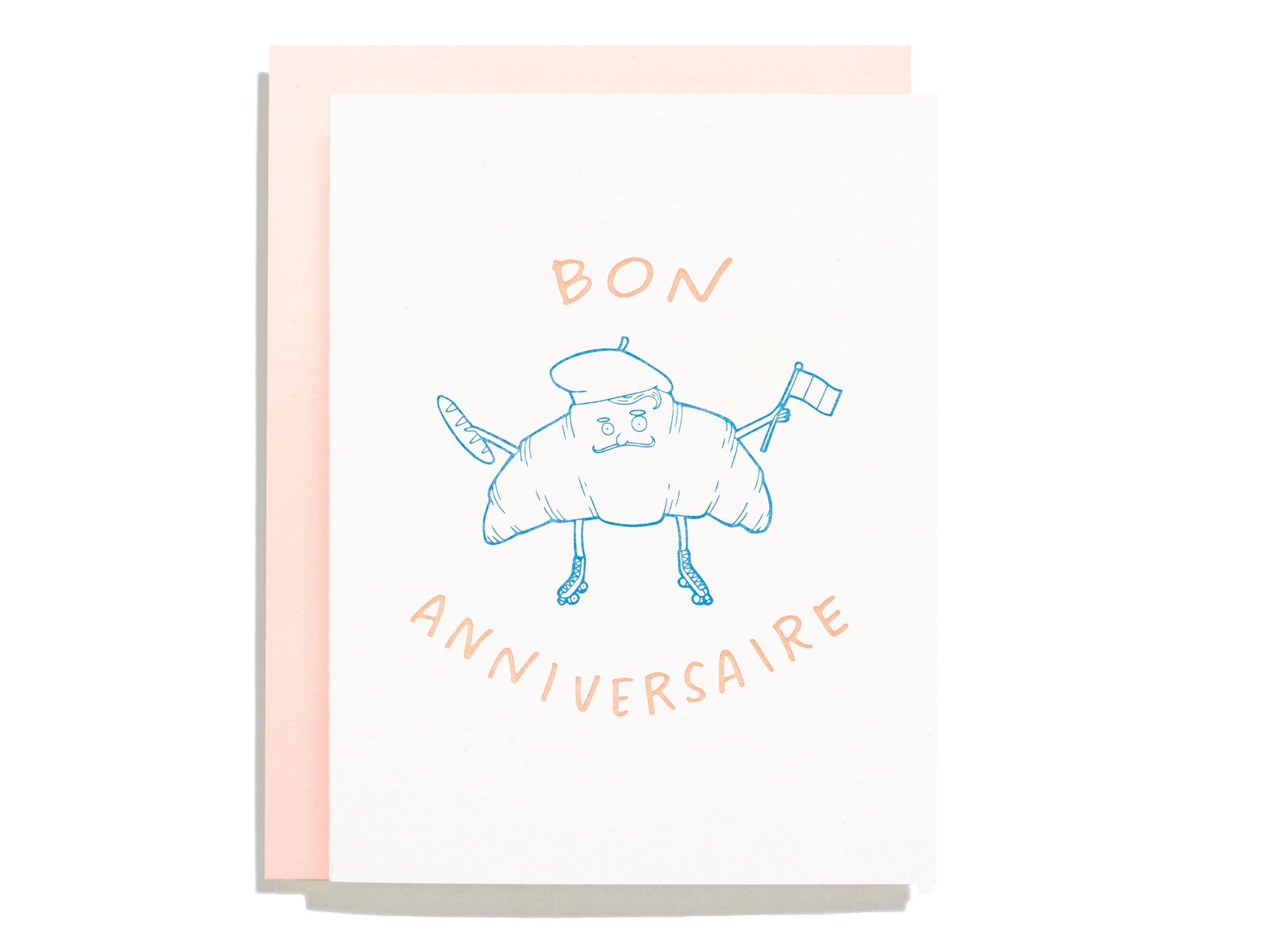 A greeting card with a hand-drawn illustration of a croissant with a smiling face and the text 'Bon Anniversaire!' on a pink background.