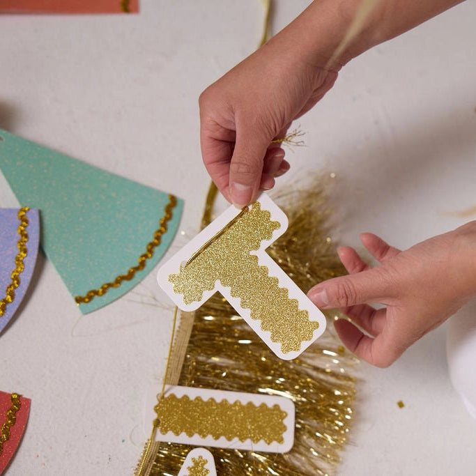 Child's hands holding a gold glittery number one cutout with colorful paper triangles in the background.