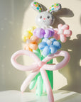 A balloon bouquet featuring a cute, cartoon-style bunny balloon with a bow, surrounded by various round balloons in pastel colors.