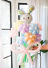 A balloon bouquet featuring a cute, cartoon-style bunny balloon with a bow, surrounded by various round balloons in pastel colors.
