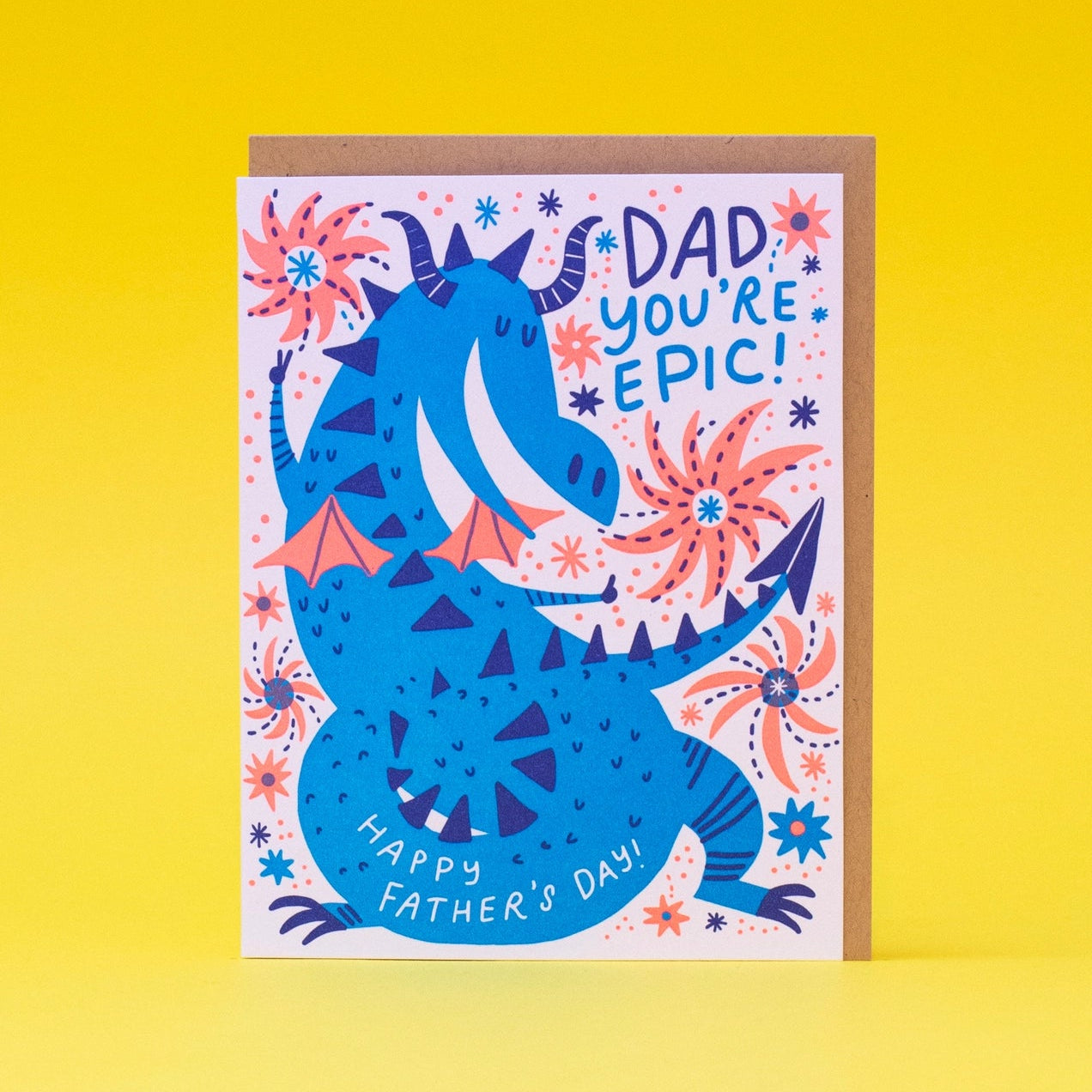 A colorful greeting card with an illustration of a dragon, floral patterns, and the text 'DAD YOU'RE EPIC! HAPPY FATHER'S DAY' on a yellow background. The card is presented with a kraft envelope.