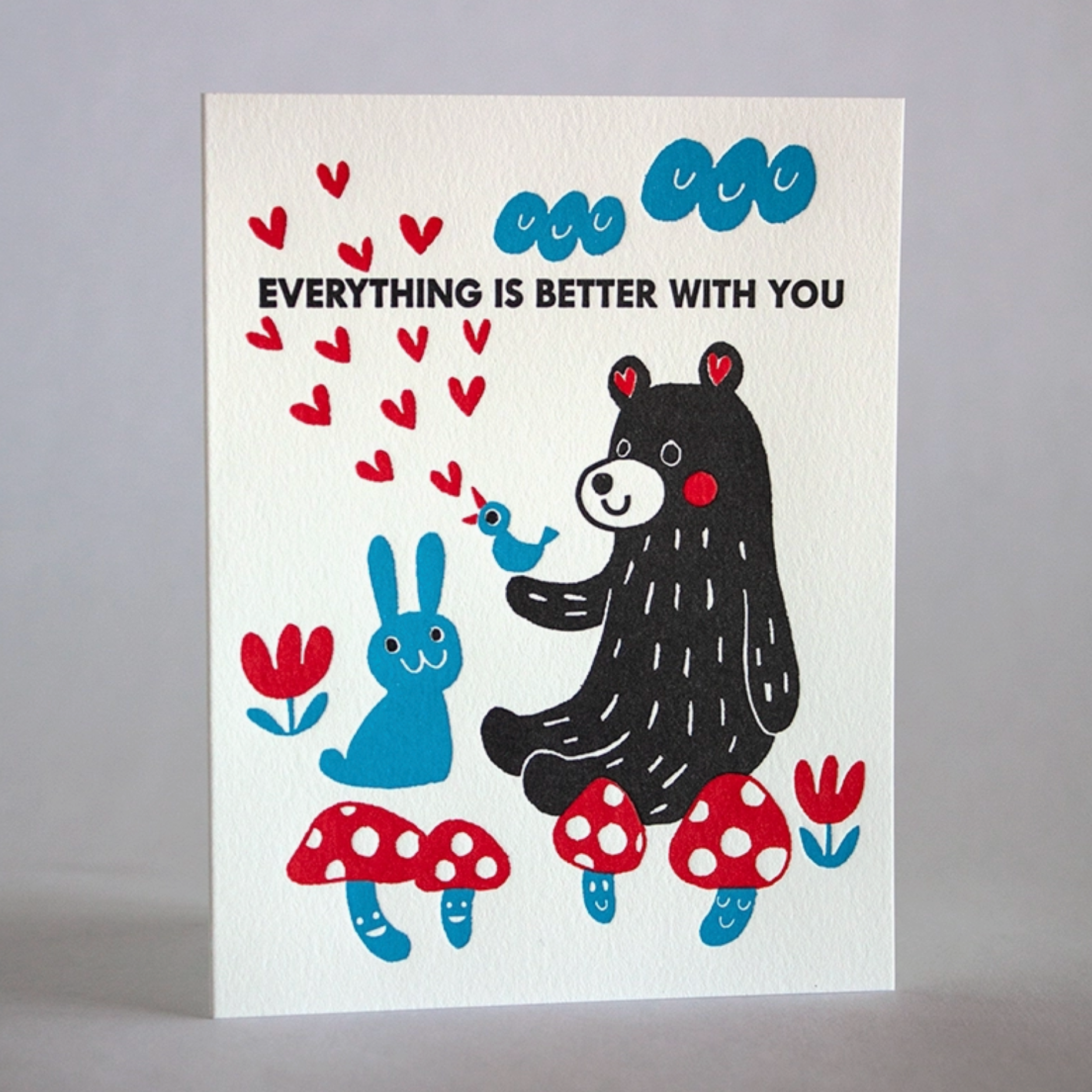 Greeting card with a rabbit, bird and bear sitting amongst flowers and mushrooms under the clouds. Text reads "Everythign is better with you"