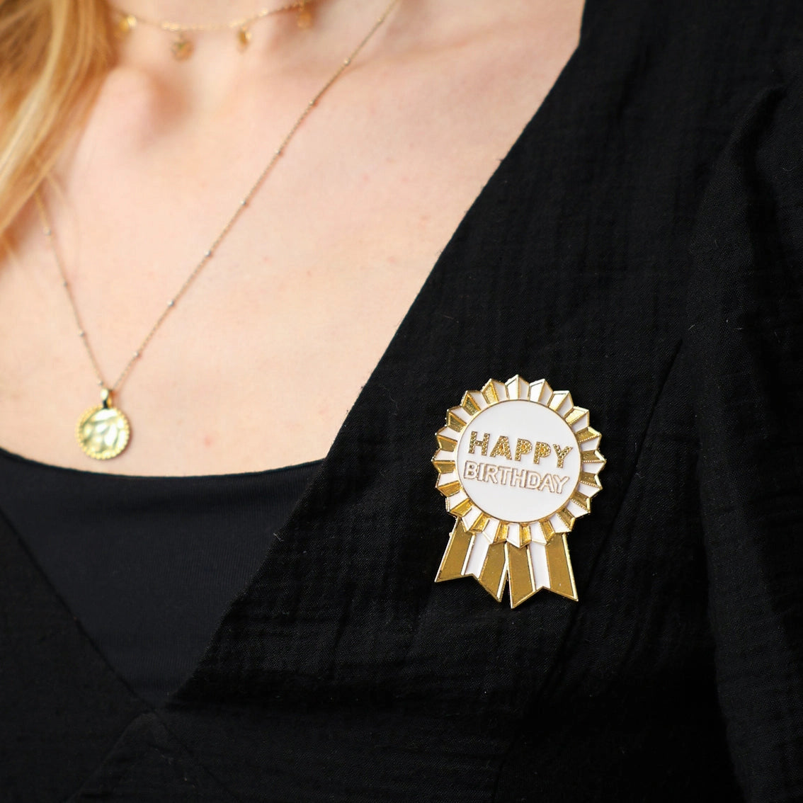 Gold and white 'Happy Birthday' ribbon pin on a black shirt