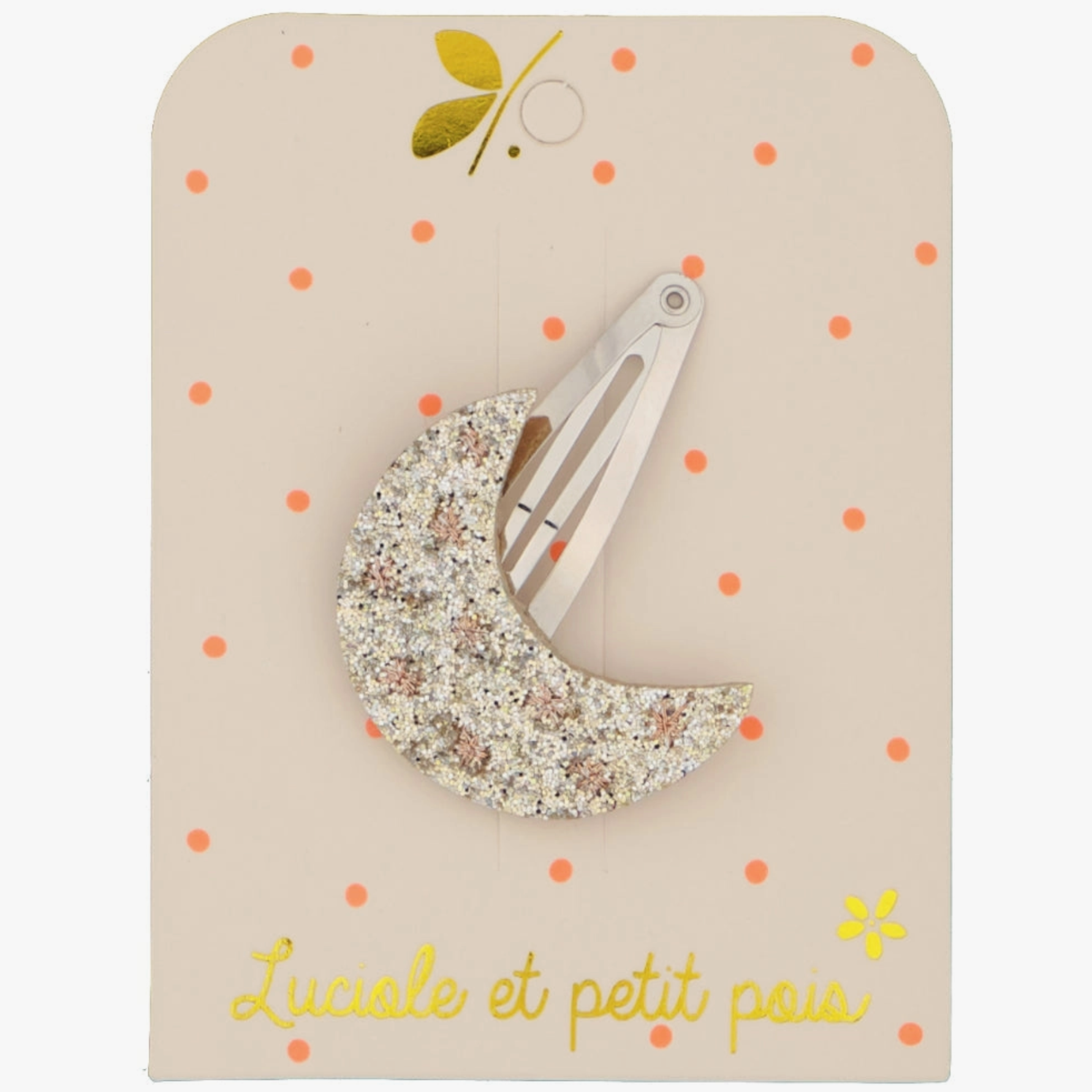 A hair clip with a golden moon and glitter details on a beige background with polka dots.
