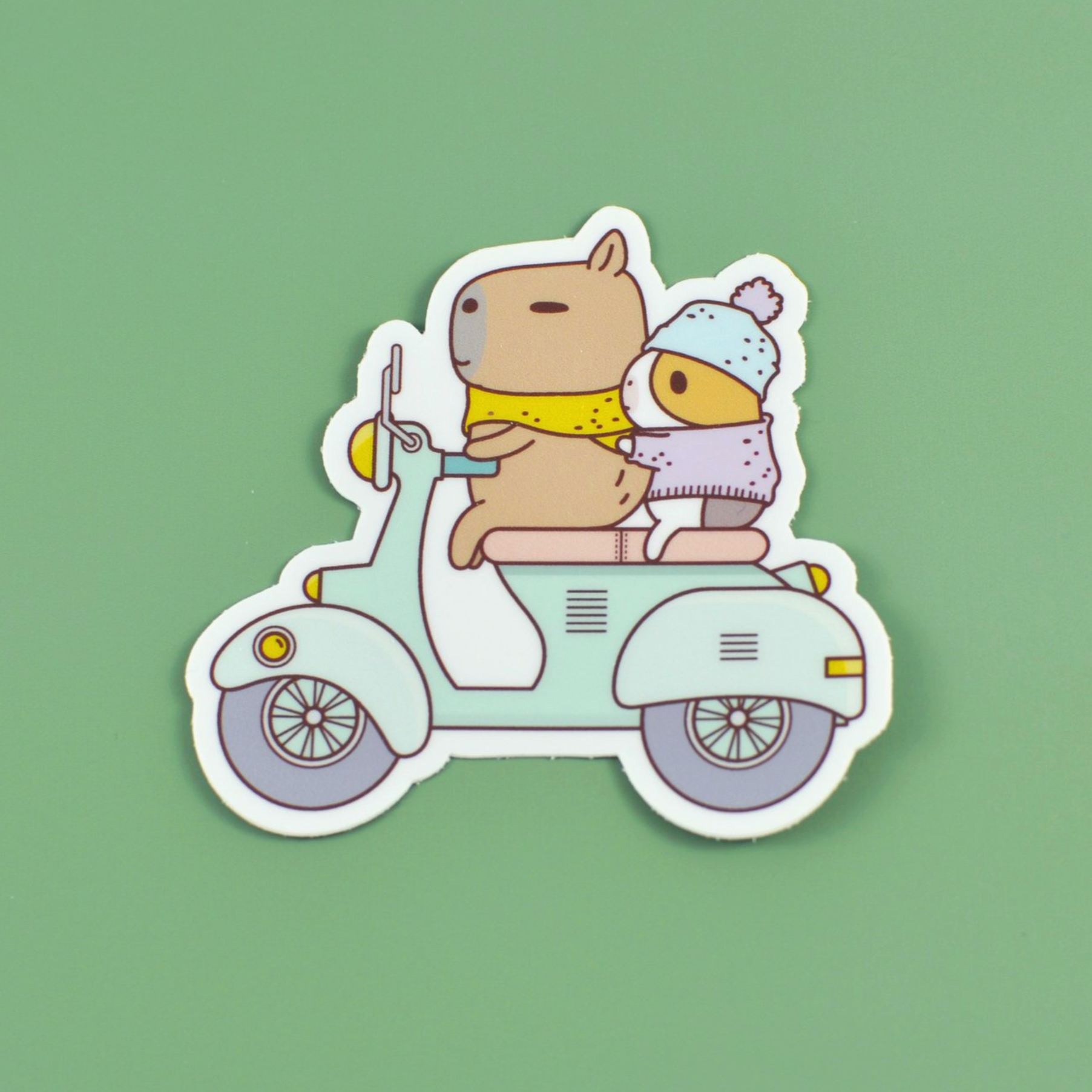 A vinyl sticker of a guinea pig and capybara riding a scooter on a green background.