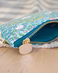 A side view of amulticolored coin purse with a brass zipper and a metal key ring, featuring a pattern of hamsters, flowers, and leaves on a fabric accent background.