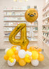 A personalized golden balloon cloud with the number 4 and a cartoonish face, displayed in a retail setting with other balloons and decorations.