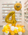 A personalized golden balloon cloud with the number 4 and a cartoonish face, displayed in a retail setting with other balloons and decorations.