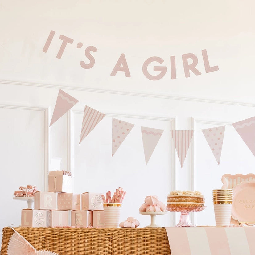 Decorated table for a baby girl shower with 'It's a Girl' banner pennant flags and decorations
