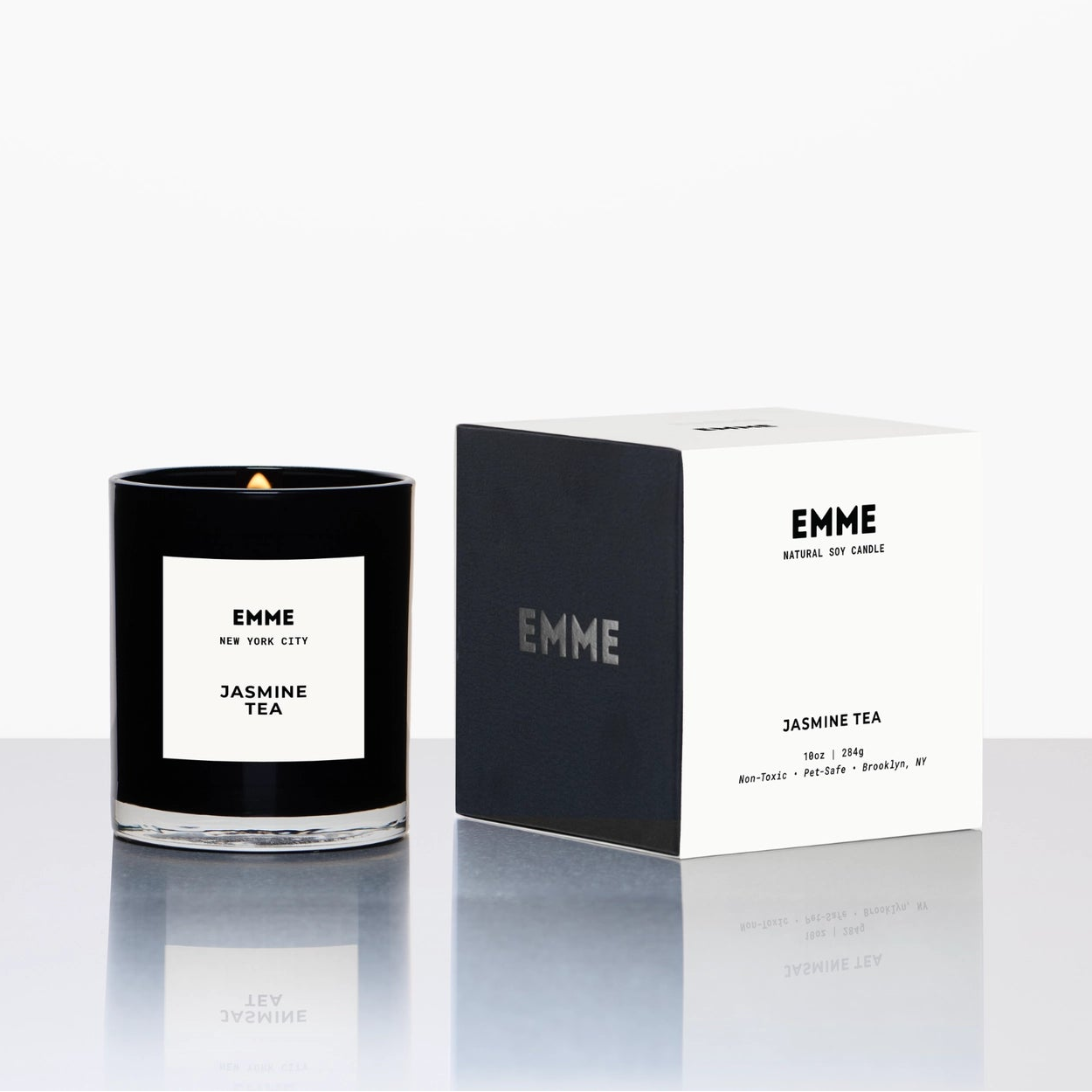 Black candle with white label and 'EMME' branding next to its box packaging on a white background