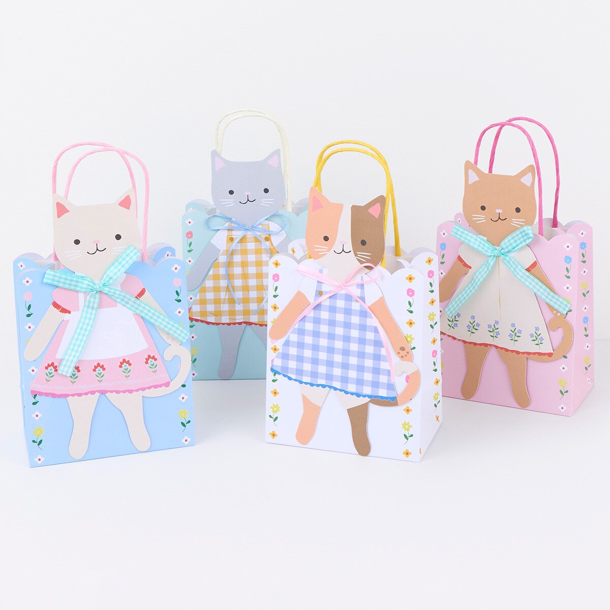 Set of four cat-themed gift bags with colorful dresses on a white background