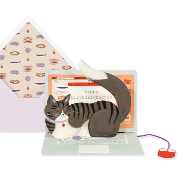 A pop-up birthday card with an illustration of a cat sitting on a laptop, with a birthday message visible on the screen. The card is accompanied by an envelope with a patterned design.