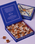 Open blue box filled with caramels and a smaller decorative box on a light purple background