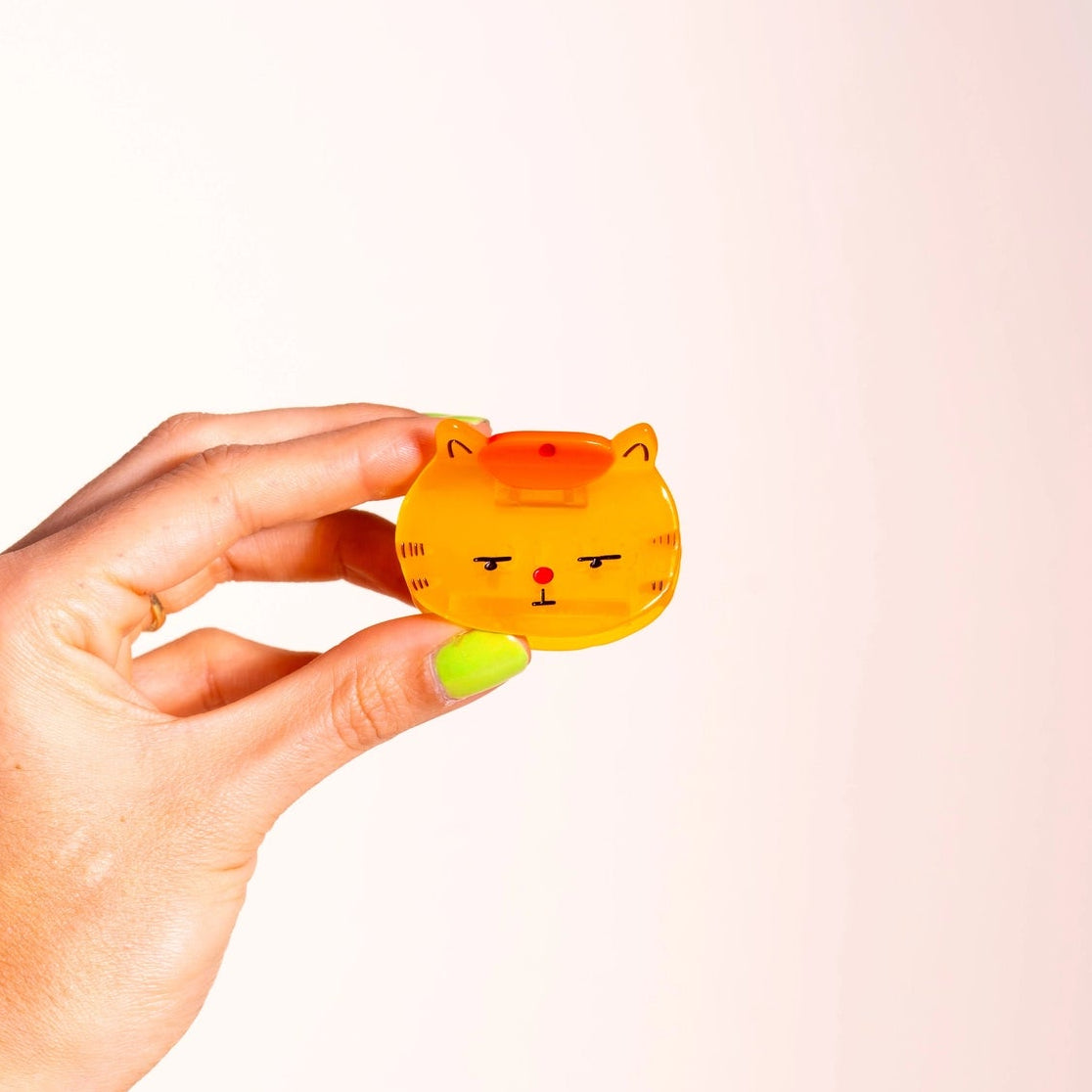 hand holding an orange cat hair clip wearing a beret, on pink background