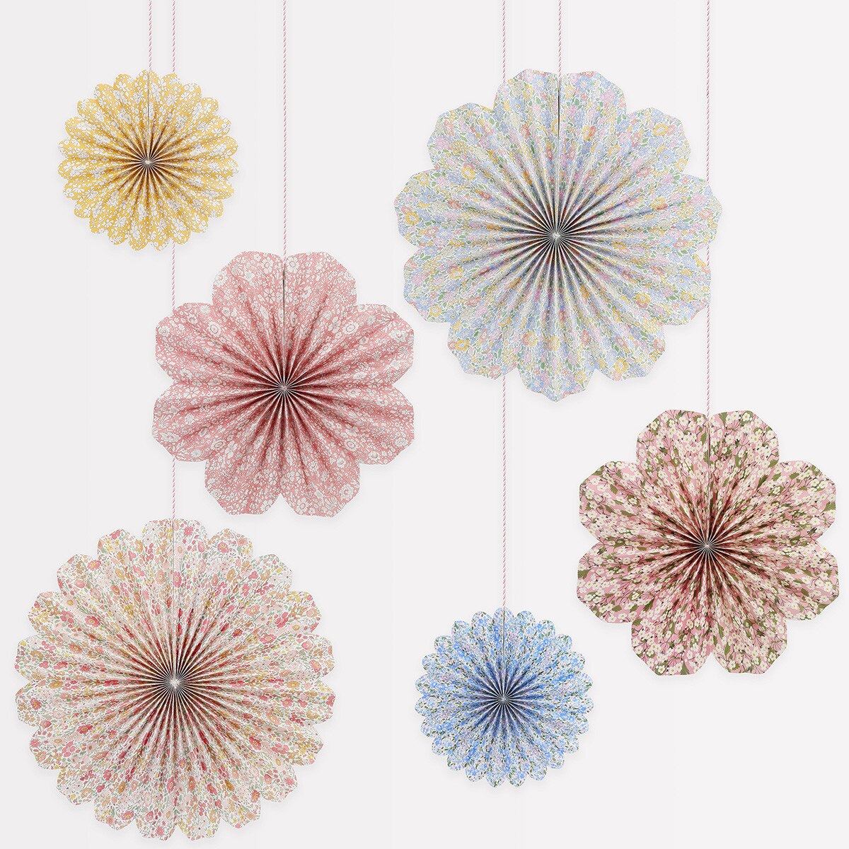 Decorative paper fans in assorted colors with floral patterns hanging against a white background