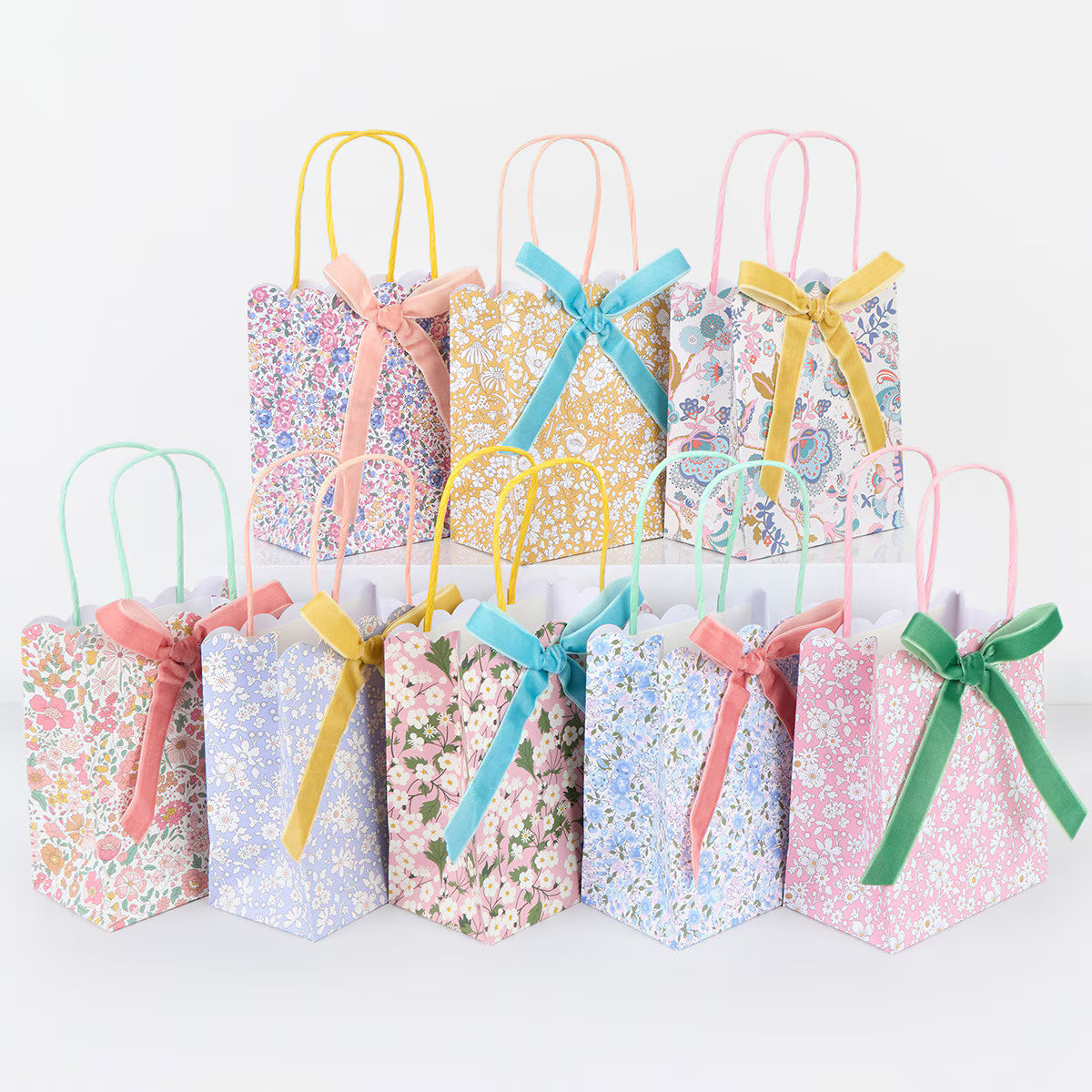 Set of small gift bags with floral patterns and colorful ribbons on a white background