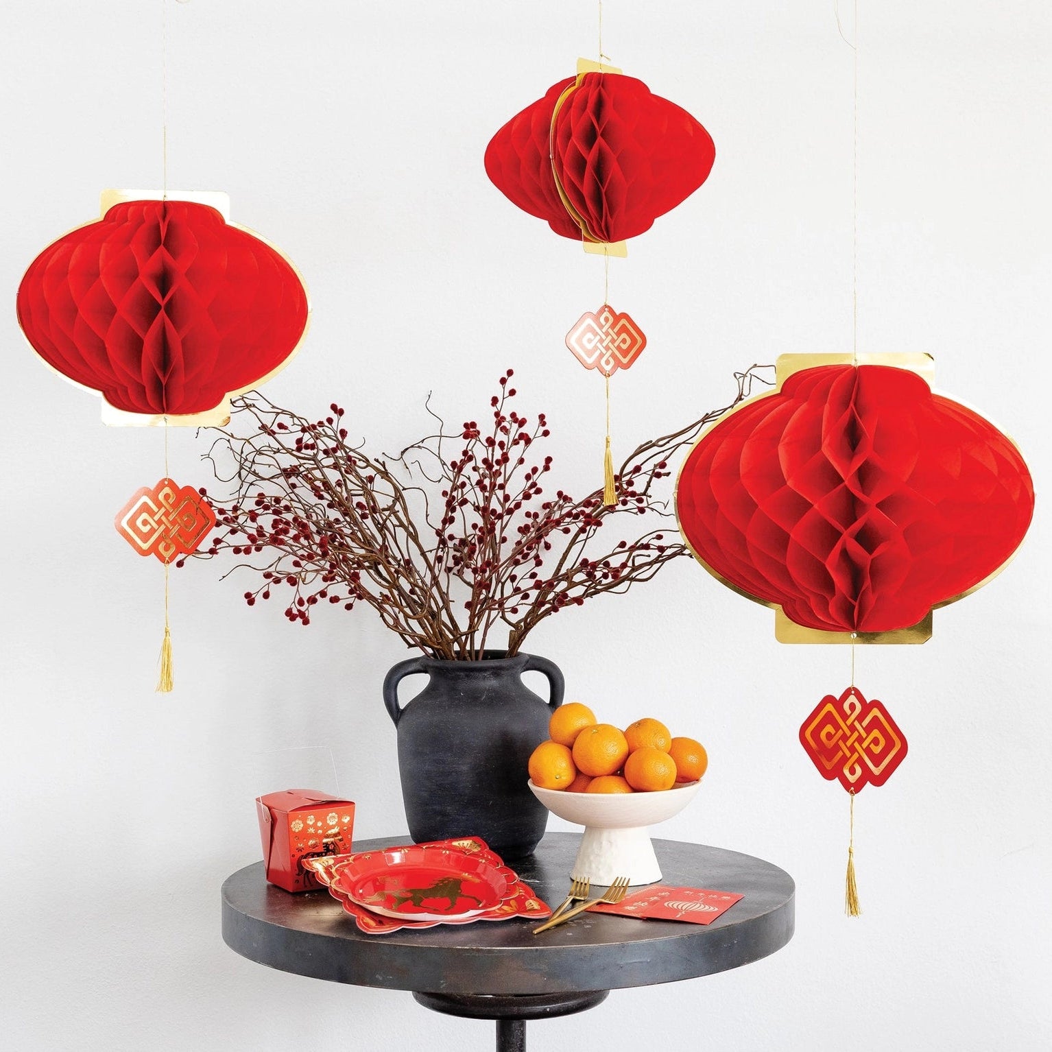 Decorative table setting with red lanterns, fruits, and a vase on a white background