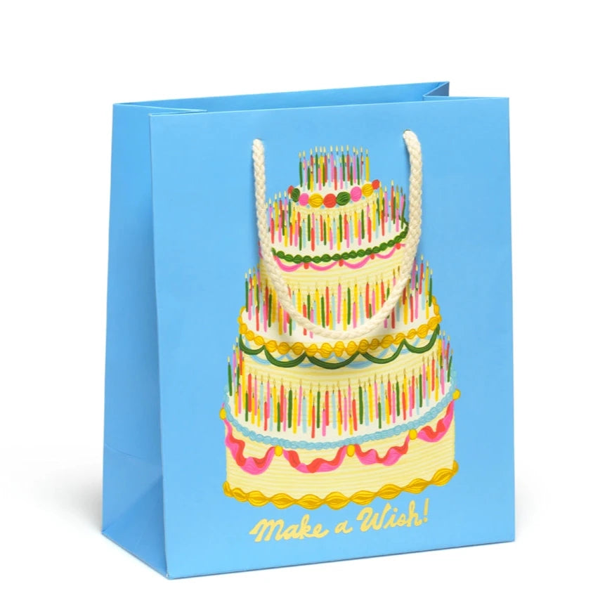 Blue gift bag with a large colorful cake filled with candles on it. Gold text that reads "Make a Wish!"