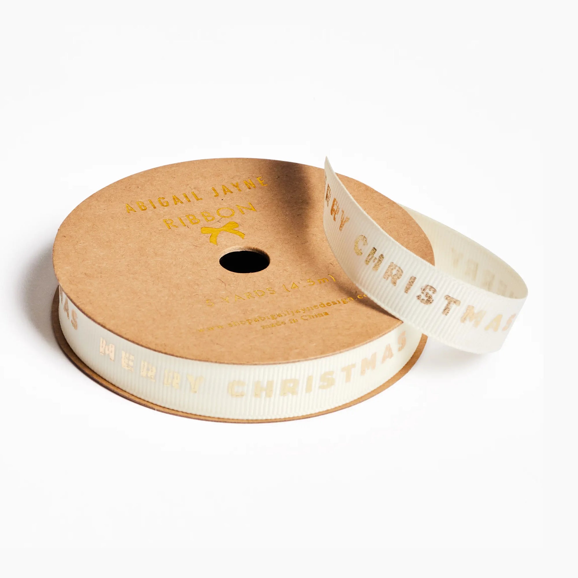 A spool of white ribbon with gold foil lettering that reads 'MERRY CHRISTMAS' 