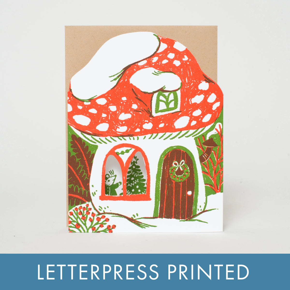 A letterpress printed greeting card featuring a whimsical mushroom house illustration in red, white, green, and brown, shown against a light gray background with a blue banner at the bottom reading 'LETTERPRESS PRINTED'.