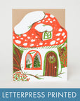 A letterpress printed greeting card featuring a whimsical mushroom house illustration in red, white, green, and brown, shown against a light gray background with a blue banner at the bottom reading 'LETTERPRESS PRINTED'.