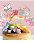 A cake topped with a Miffy-themed topper, featuring cartoon-style rabbit characters and birthday greetings.