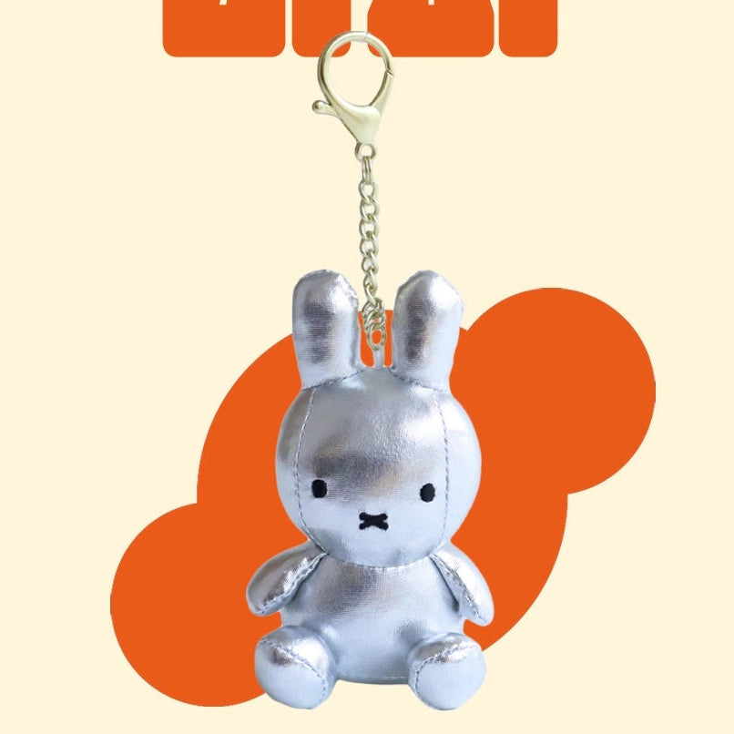 Silver plush bunny keychain on a beige background with orange shapes