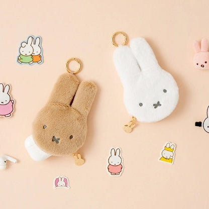 Two plush keychains, one brown and one white, on a beige background with cartoon illustrations of bunnies.