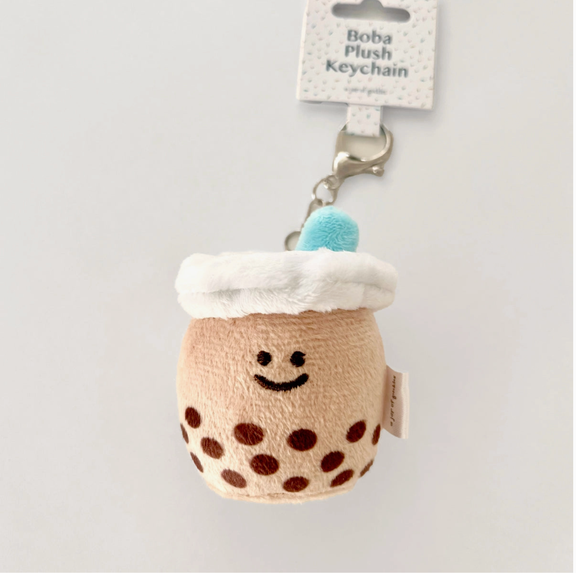 A plush keychain designed to look like a boba tea drink with a smiling face, brown sugar dots, and a blue straw on top.