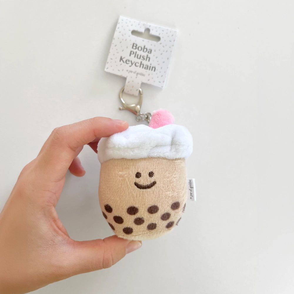 A plush keychain designed to look like a boba tea drink with a smiling face, brown sugar dots, and a blue straw on top.