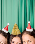 Three women wearing festive hats against a green curtain