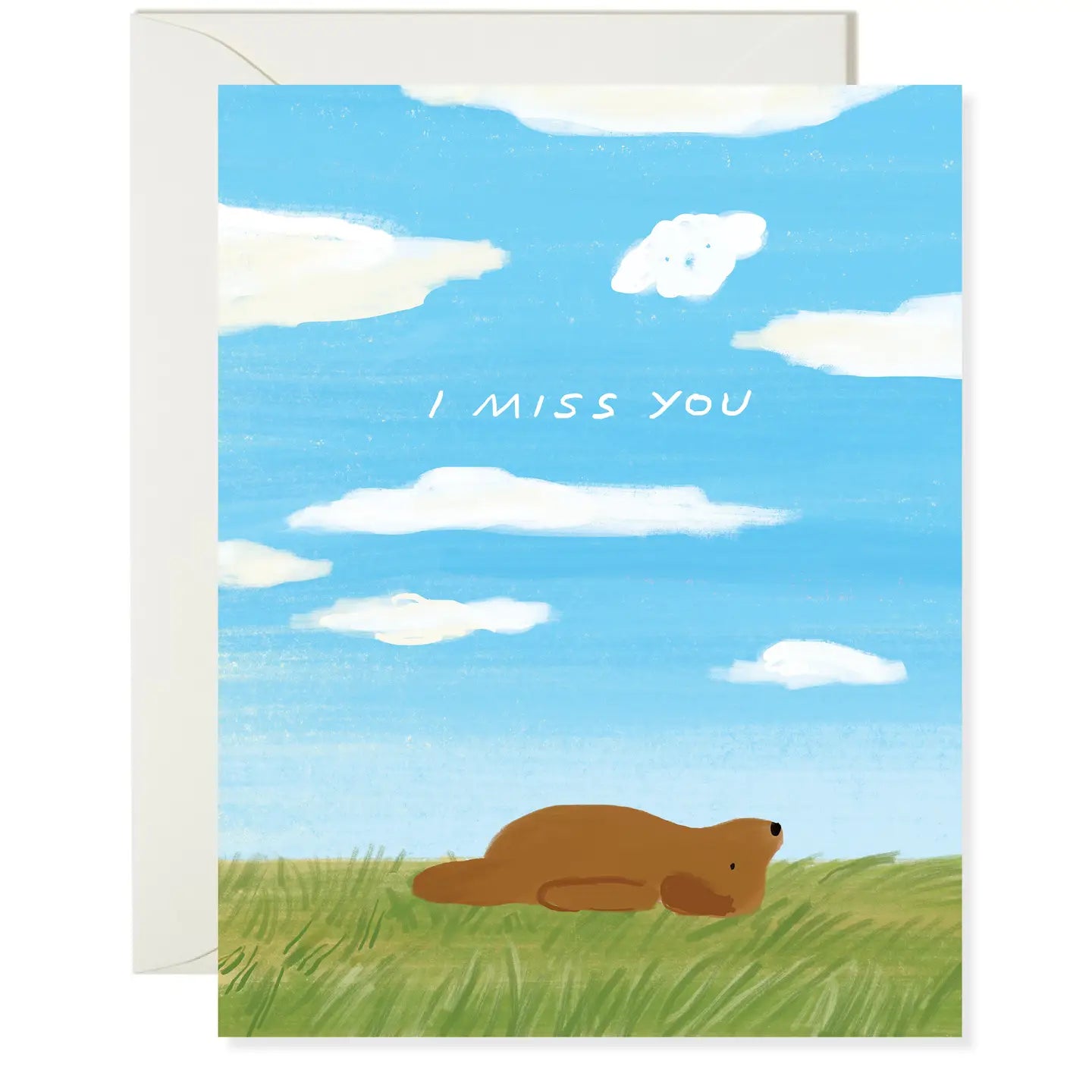 A greeting card with a blue sky and clouds background, featuring an illustration of a dog lying down, with the text 'I MISS YOU' on the front.