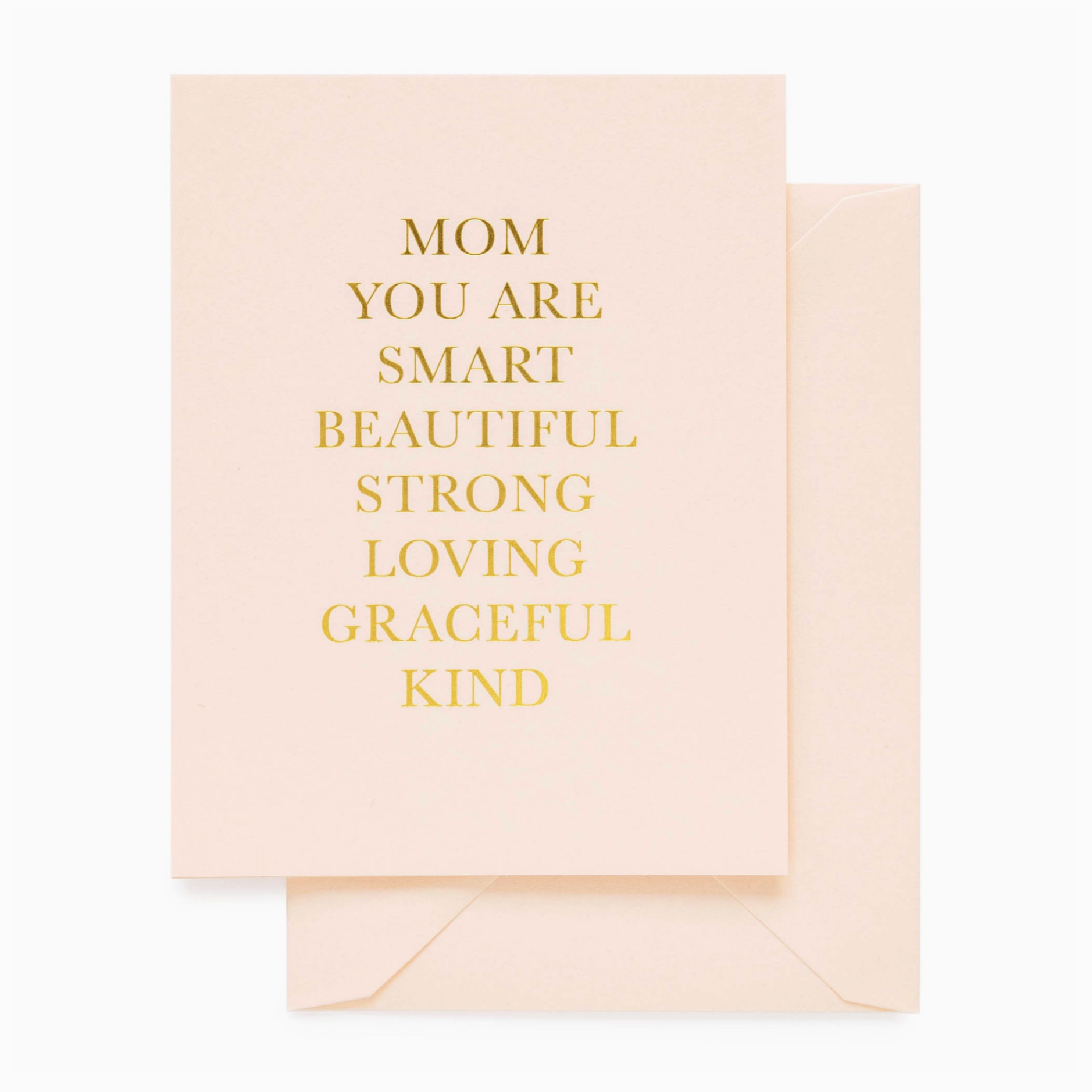 A pink greeting card with gold foil text that reads 'Mom you are smart, beautiful, strong, loving, graceful, and kind.' The card is presented with a matching envelope.