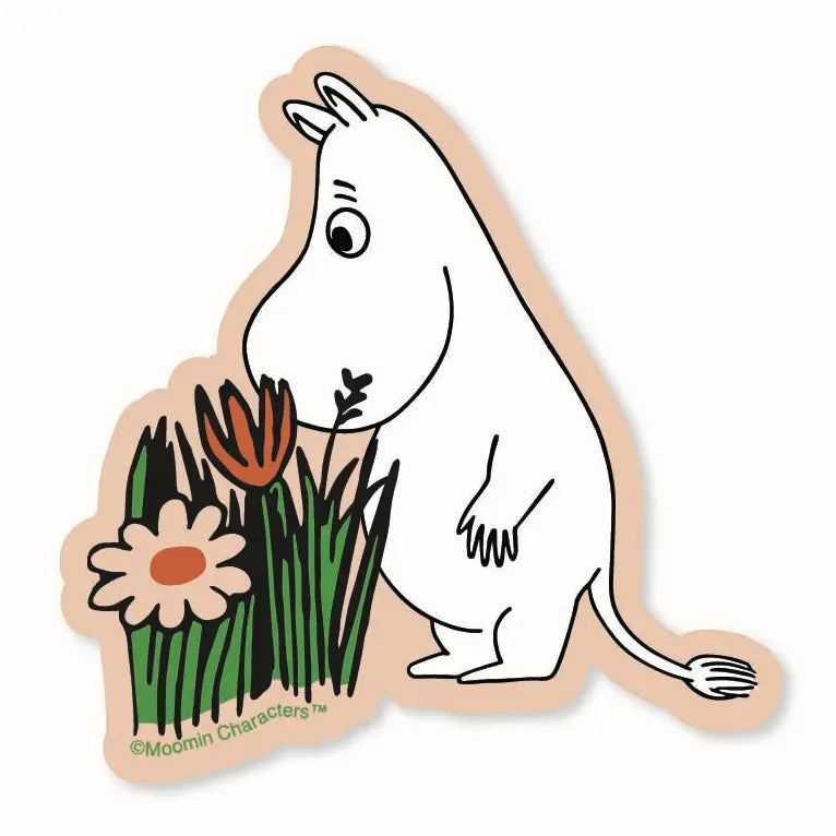 A die-cut sticker featuring the Moomin character Moomi in a white body, sniffing green grass with flowers, on a light beige background. 