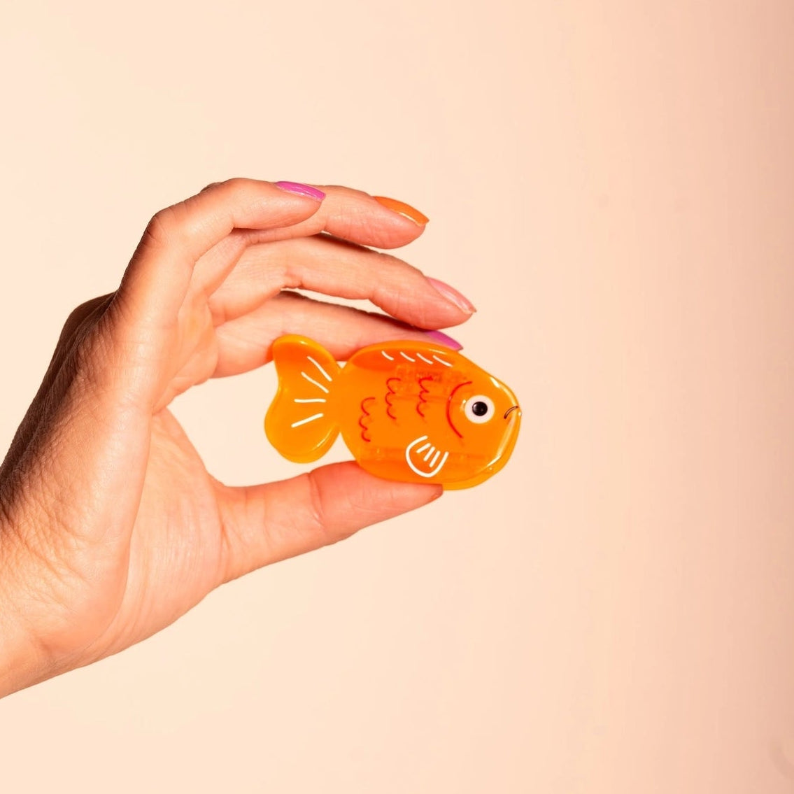 hand holding fish shaped orange hair claw clip, on coral background