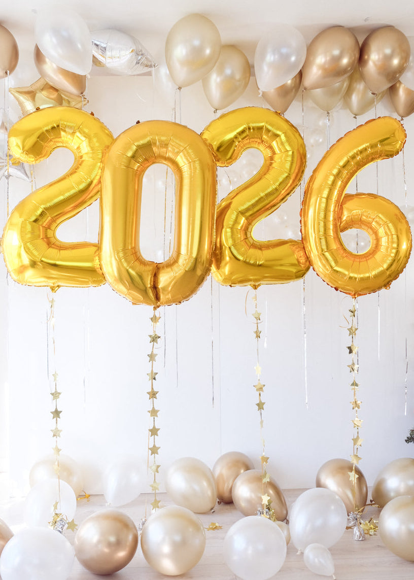 Gold '2026' balloons with white and gold balloons on a light wooden floor.
