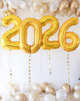 Gold '2026' balloons with white and gold balloons on a light wooden floor.