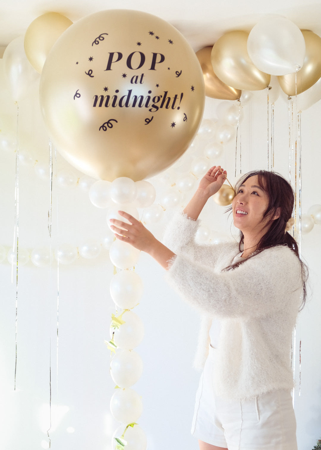 Woman holding a balloon with 'Pop at midnight!' text in a decorated room.